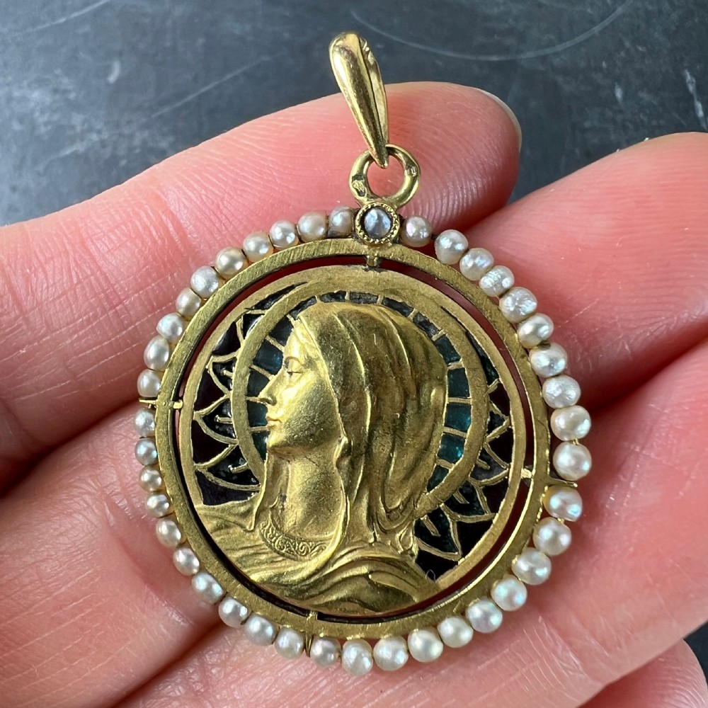 An 18k gold circular pendant featuring a sculpted profile of the Virgin Mary surrounded by translucent blue and green plique-a-jour enamel and framed by seed pearls. View X
