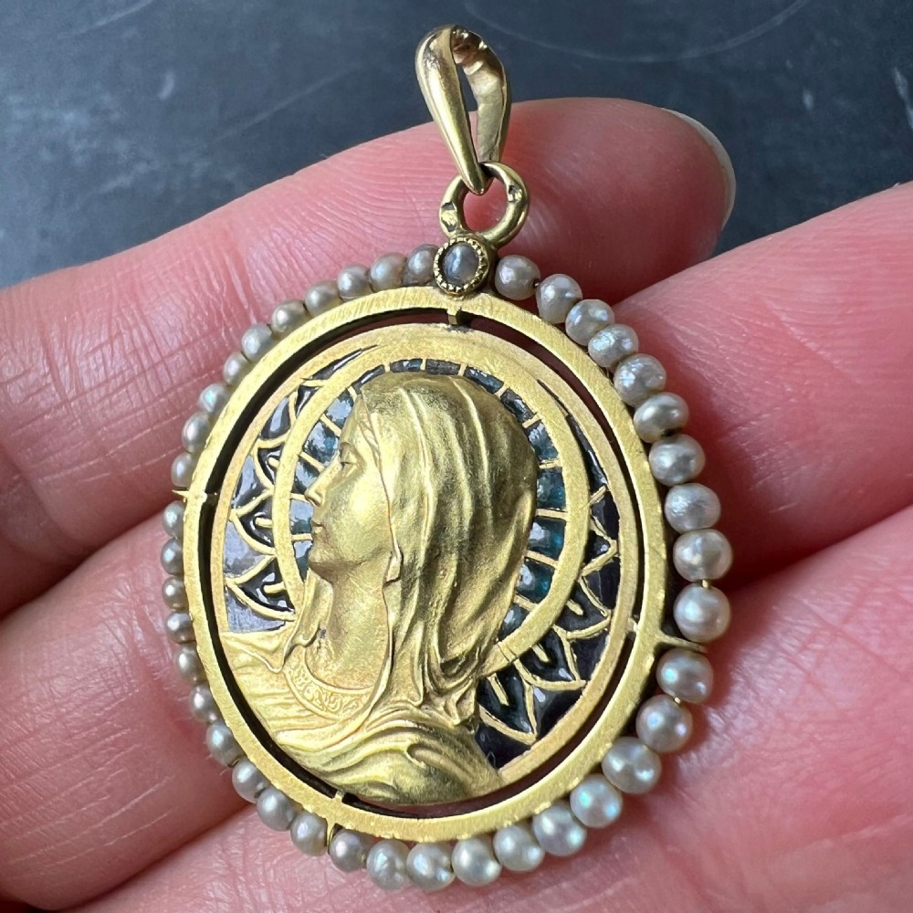 An 18k gold circular pendant featuring a sculpted profile of the Virgin Mary surrounded by translucent blue and green plique-a-jour enamel and framed by seed pearls. View XI