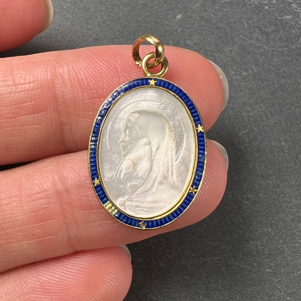 An oval 18-carat yellow gold pendant featuring a carved mother-of-pearl profile of the Virgin Mary encircled by a royal blue enamelled border with gold stars. View V