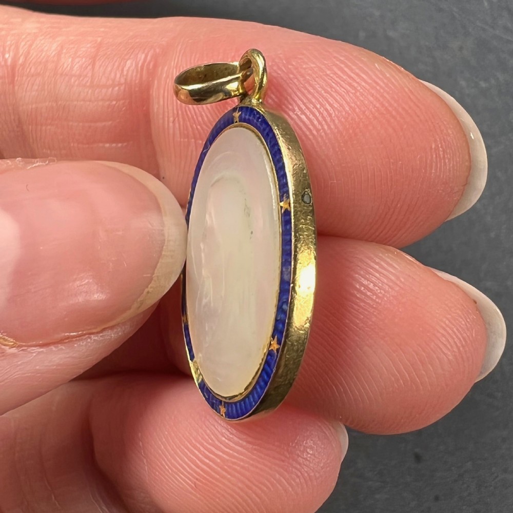 An oval 18-carat yellow gold pendant featuring a carved mother-of-pearl profile of the Virgin Mary encircled by a royal blue enamelled border with gold stars. View VI