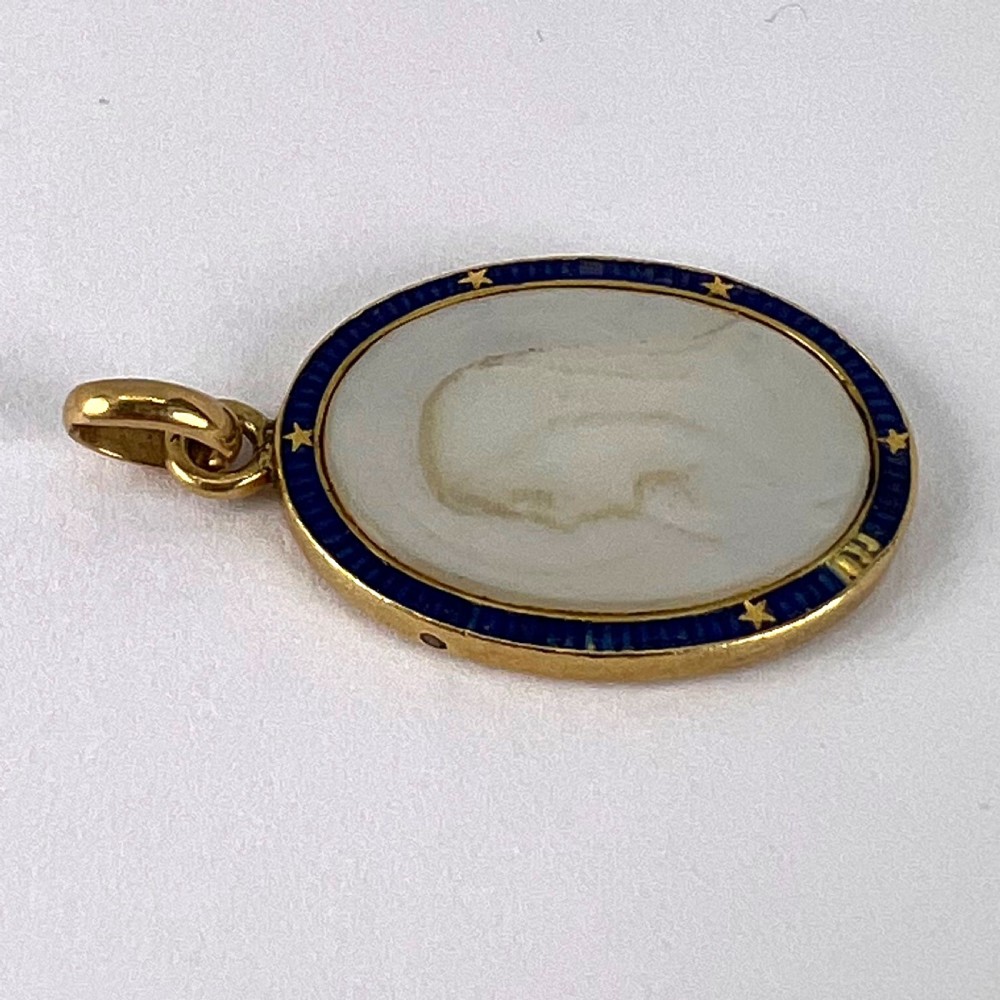 An oval 18-carat yellow gold pendant featuring a carved mother-of-pearl profile of the Virgin Mary encircled by a royal blue enamelled border with gold stars. View X