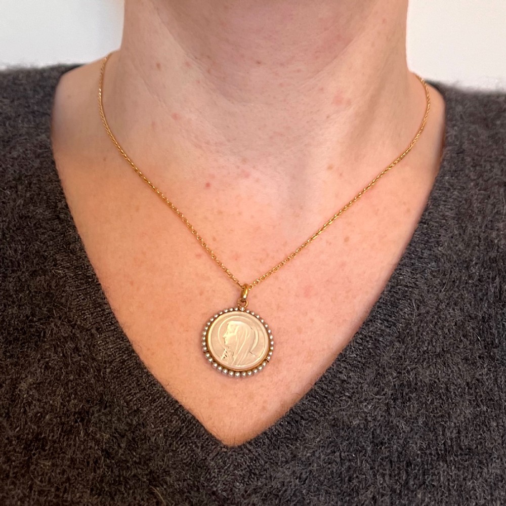 A circular gold pendant featuring a carved mother of pearl profile of the Virgin Mary encircled by seed pearls. View IV