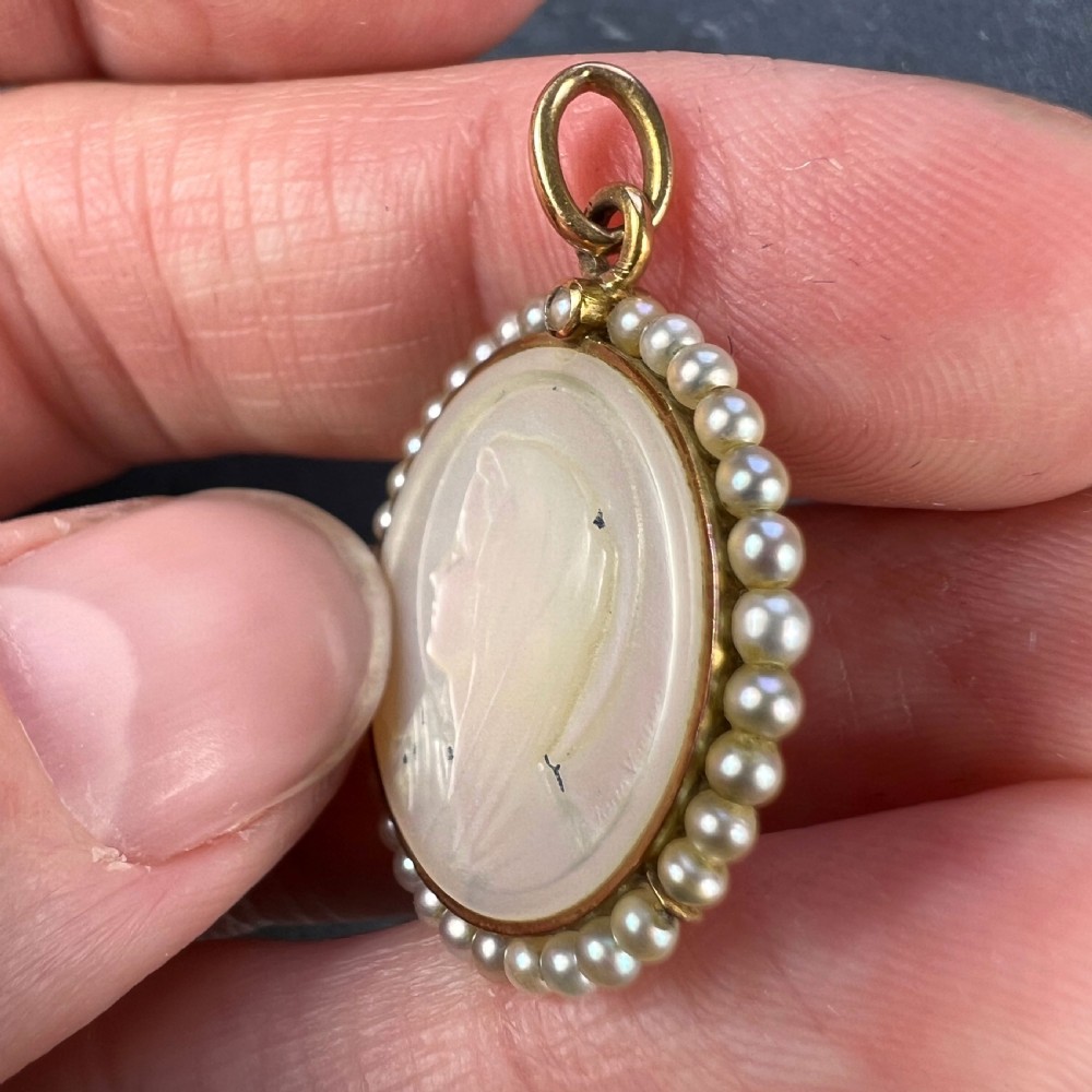 A circular gold pendant featuring a carved mother of pearl profile of the Virgin Mary encircled by seed pearls. View VI