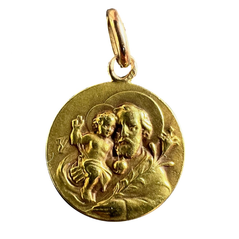 A circular 18k yellow gold medal depicting Saint Joseph holding the Infant Jesus and a lily branch in raised relief with a top suspension loop.