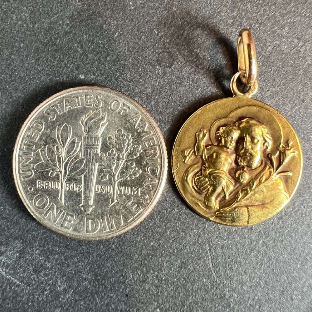 A circular 18k yellow gold medal depicting Saint Joseph holding the Infant Jesus and a lily branch in raised relief with a top suspension loop. View XI