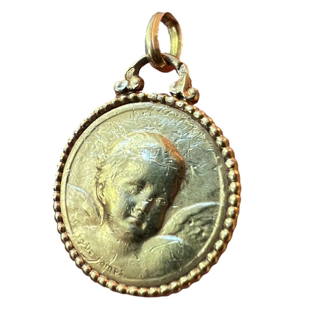 A round 18K yellow gold medal pendant featuring a bas-relief motif of a cherub head framed by a beaded border.