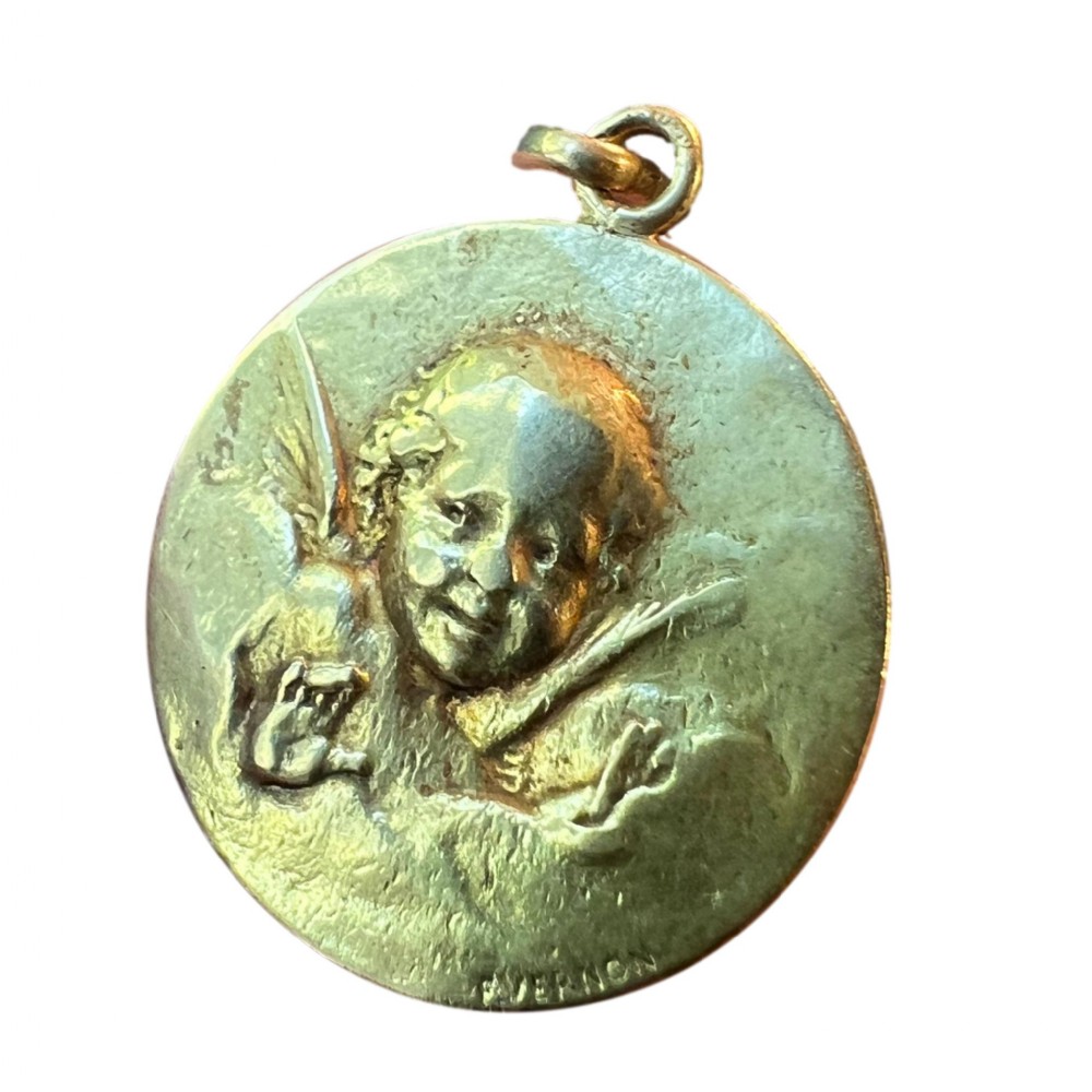 A circular 18ct yellow gold medal pendant featuring a bas-relief carving of a cherub and signed F. Vernon at the bottom edge.
