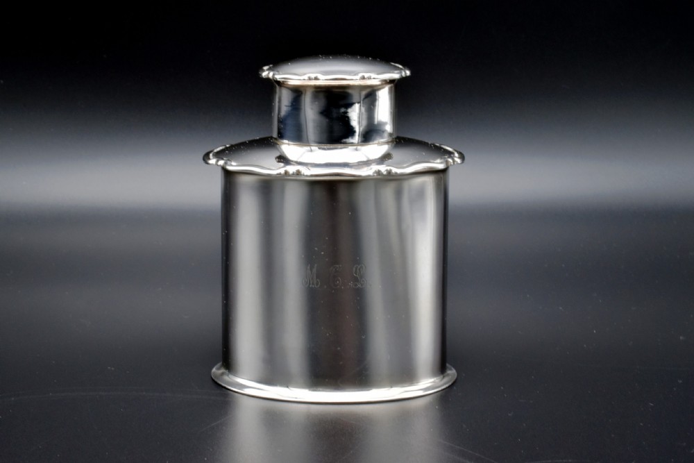 A cylindrical Edwardian sterling silver tea caddy with a scalloped edge lid and an engraved monogram on the front.