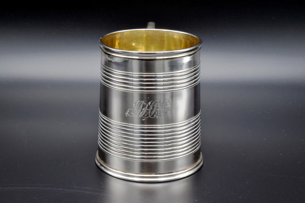 A cylindrical antique sterling silver tankard with horizontal reeded bands, a sculpted C-scroll handle, stamped hallmarks near the upper rim, and a gilded interior. View II