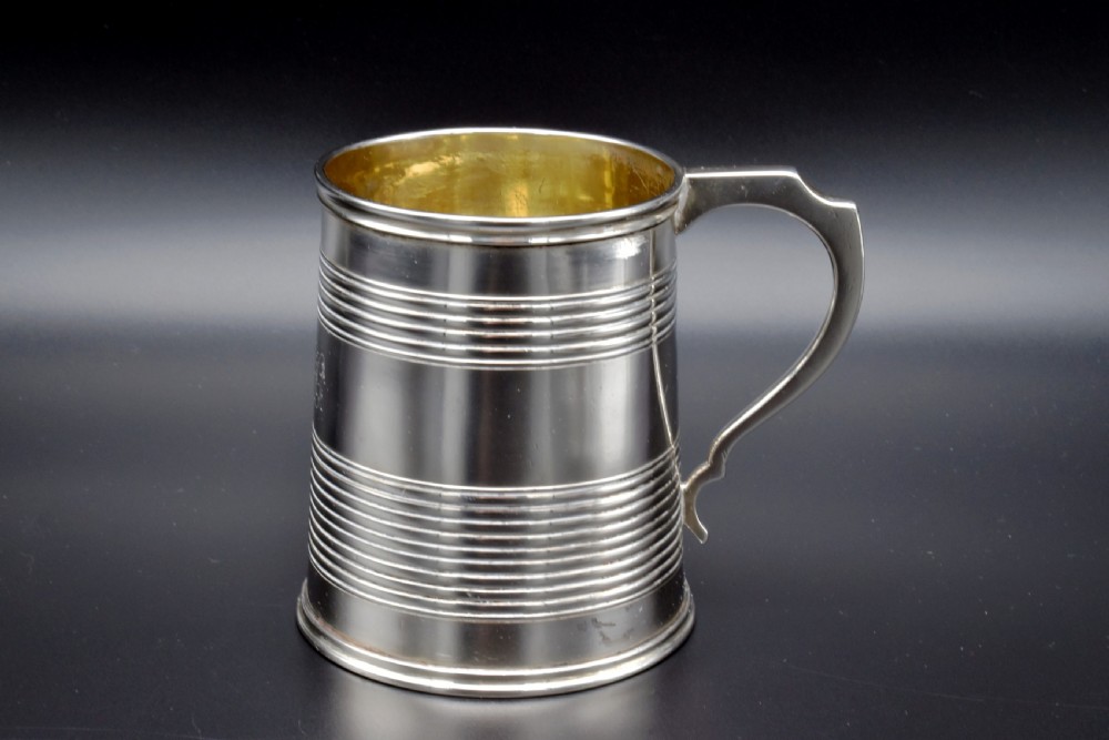A cylindrical antique sterling silver tankard with horizontal reeded bands, a sculpted C-scroll handle, stamped hallmarks near the upper rim, and a gilded interior. View III