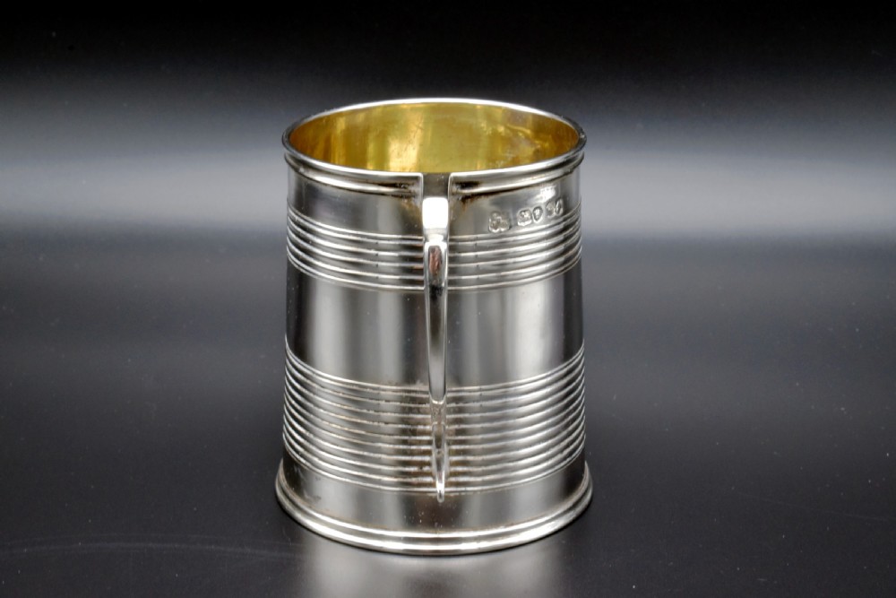 A cylindrical antique sterling silver tankard with horizontal reeded bands, a sculpted C-scroll handle, stamped hallmarks near the upper rim, and a gilded interior. View IV