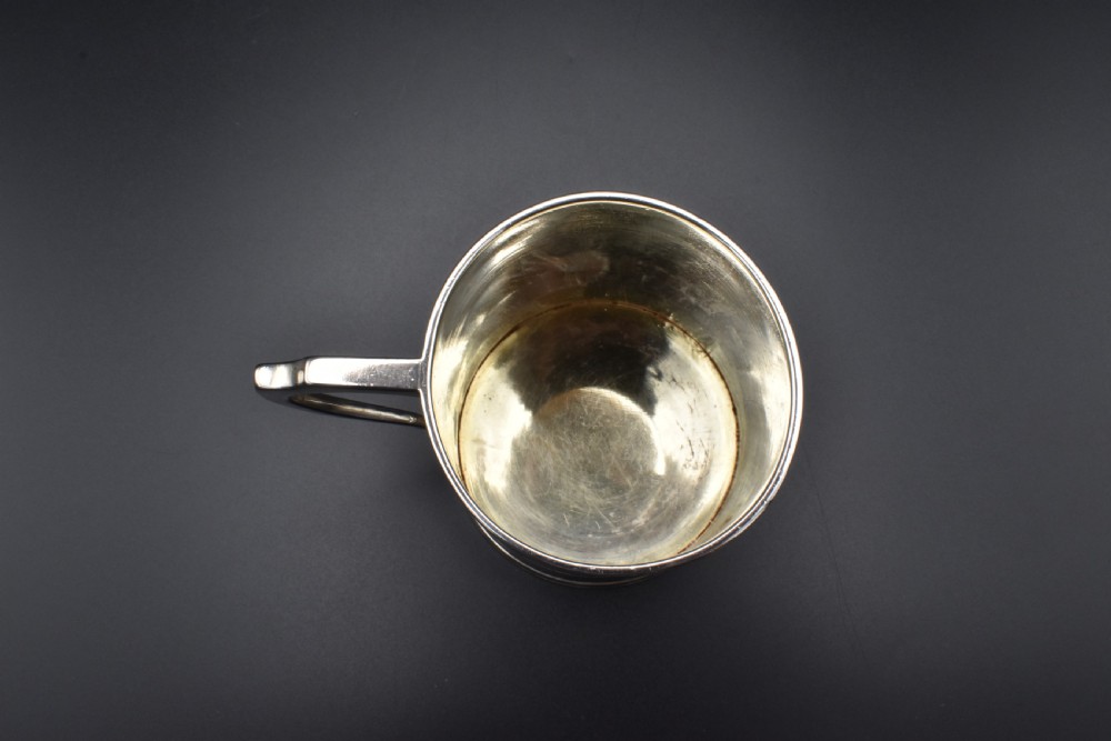 A cylindrical antique sterling silver tankard with horizontal reeded bands, a sculpted C-scroll handle, stamped hallmarks near the upper rim, and a gilded interior. View VI