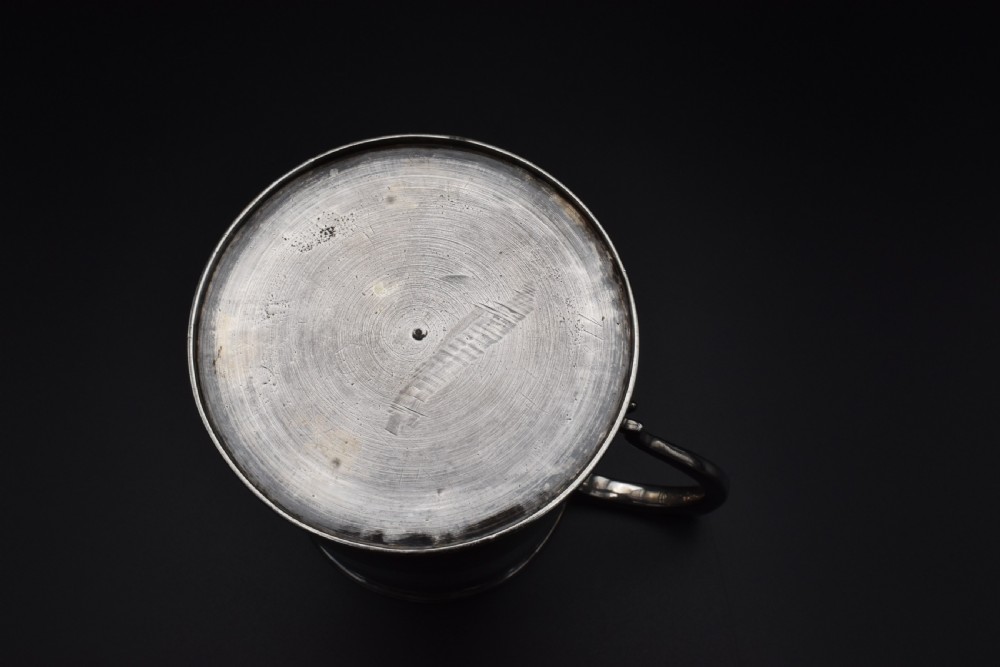 A cylindrical antique sterling silver tankard with horizontal reeded bands, a sculpted C-scroll handle, stamped hallmarks near the upper rim, and a gilded interior. View VII