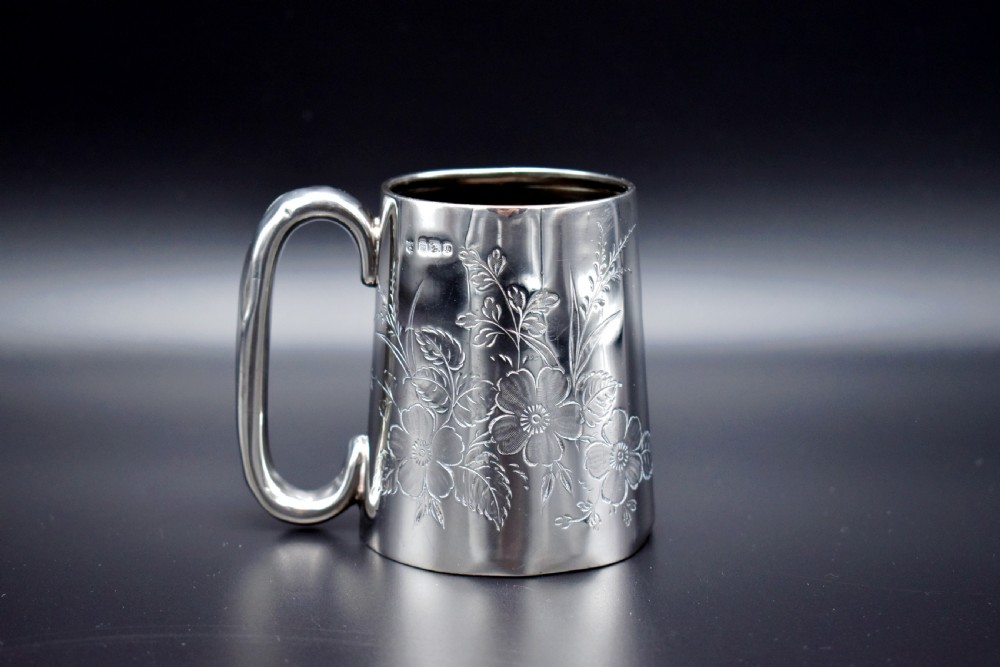 A late Victorian sterling silver tankard featuring etched floral motifs and British hallmarks near the top rim.