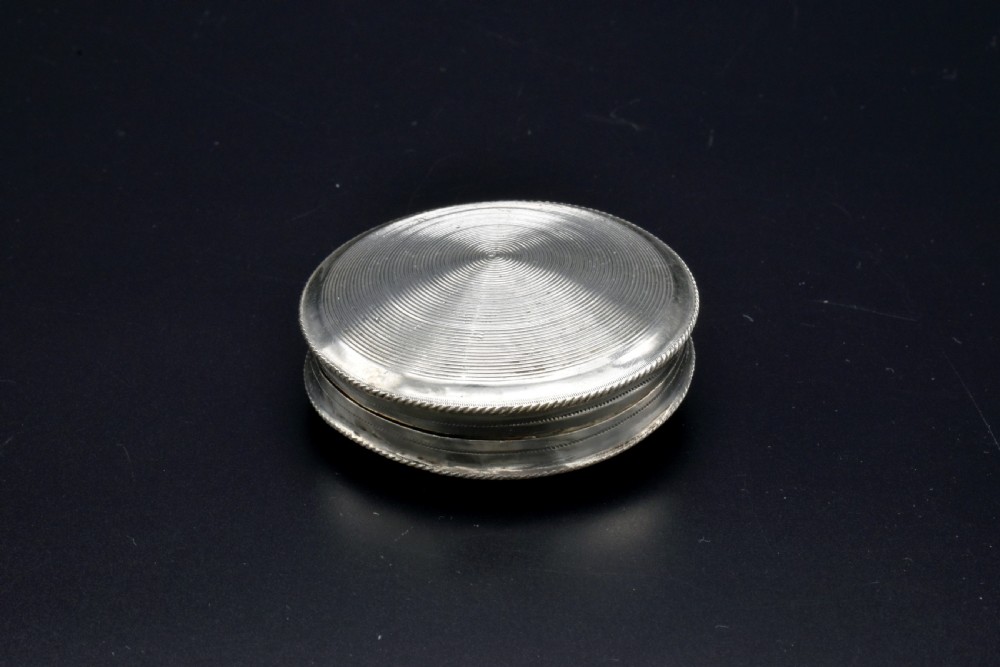 A circular 19th-century Dutch sterling silver snuff box featuring concentric engine-turned engraving and reeded borders.