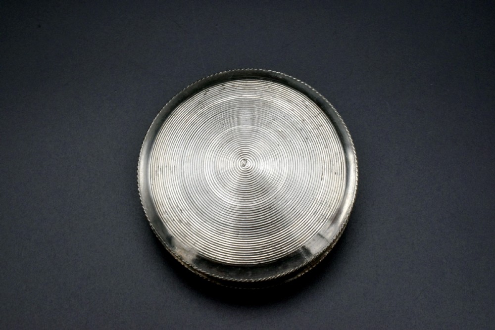 A circular 19th-century Dutch sterling silver snuff box featuring concentric engine-turned engraving and reeded borders. View II