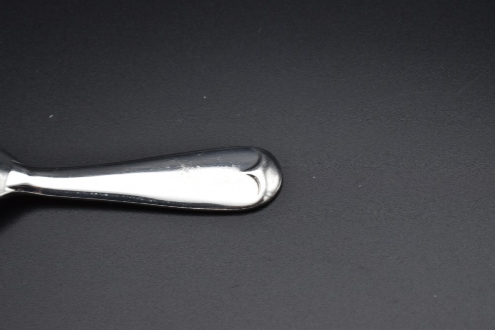 A sterling silver caddy spoon featuring a broad oval scoop bowl and a short flat handle with horizontal line accents. View IV