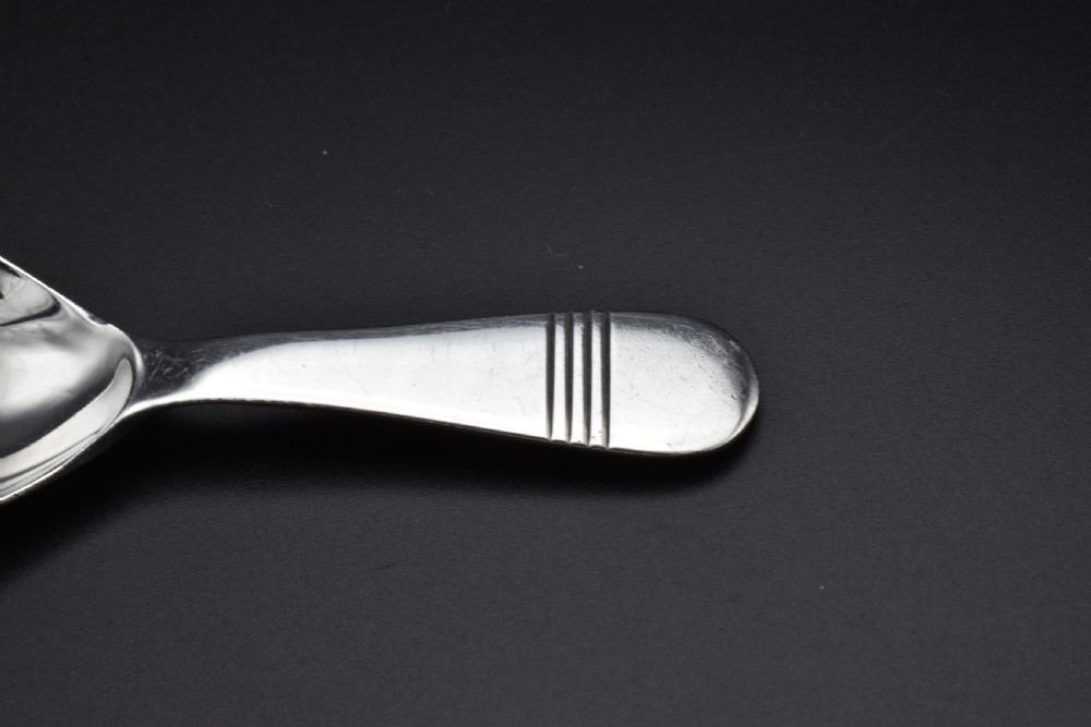 A sterling silver caddy spoon featuring a broad oval scoop bowl and a short flat handle with horizontal line accents. View V