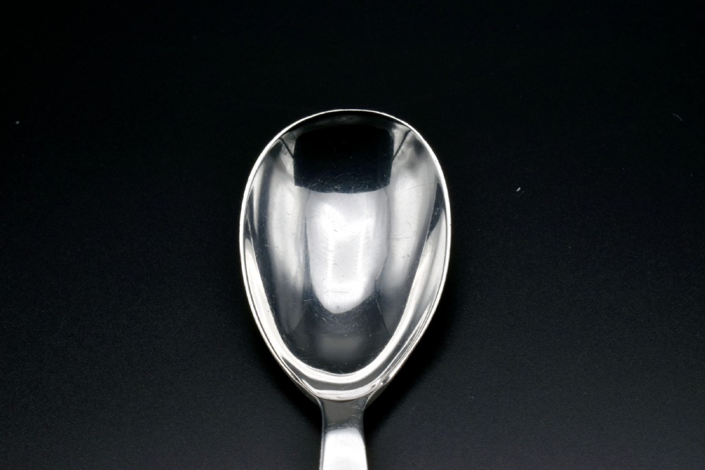 A sterling silver caddy spoon featuring a broad oval scoop bowl and a short flat handle with horizontal line accents. View VII