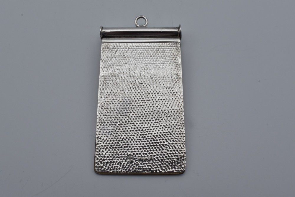 A Victorian sterling silver pocket notebook featuring a hammered finish, central monogram cartouche, top suspensory ring, and British hallmarks dated 1899. View II