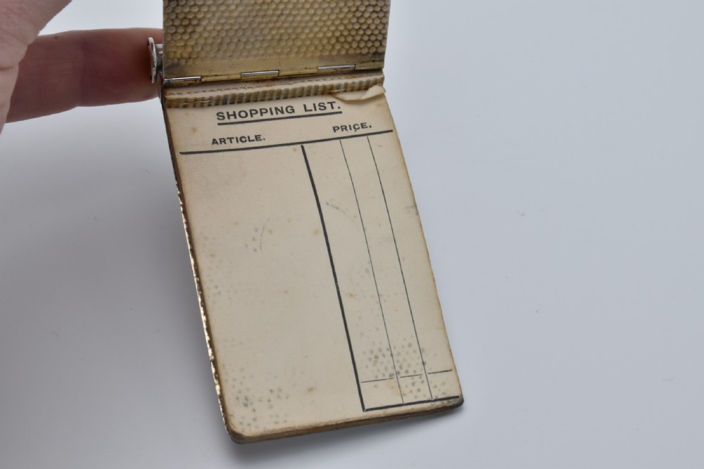 A Victorian sterling silver pocket notebook featuring a hammered finish, central monogram cartouche, top suspensory ring, and British hallmarks dated 1899. View VI