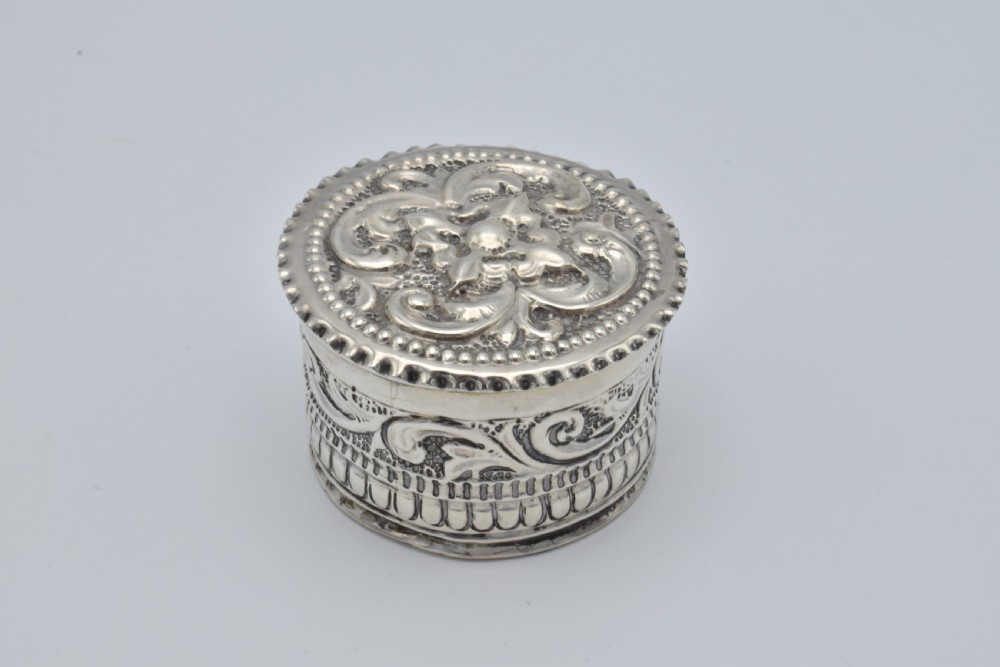 A circular Victorian sterling silver snuff box with repousse floral scrollwork on the lid and fluted sides.