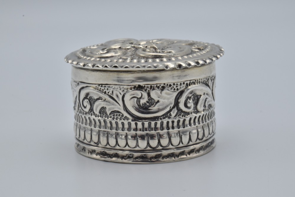 A circular Victorian sterling silver snuff box with repousse floral scrollwork on the lid and fluted sides. View II
