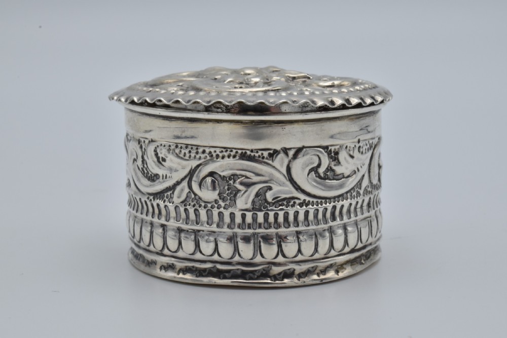 A circular Victorian sterling silver snuff box with repousse floral scrollwork on the lid and fluted sides. View III