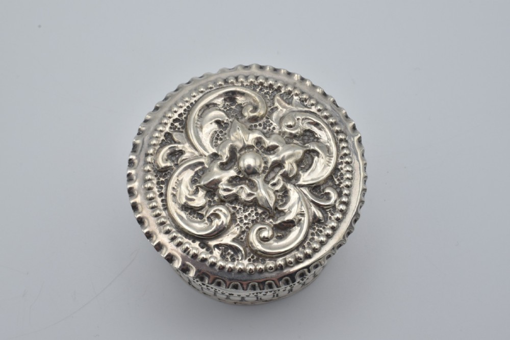 A circular Victorian sterling silver snuff box with repousse floral scrollwork on the lid and fluted sides. View IV