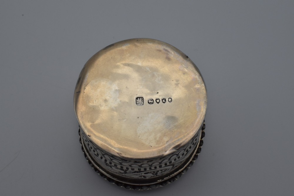 A circular Victorian sterling silver snuff box with repousse floral scrollwork on the lid and fluted sides. View V