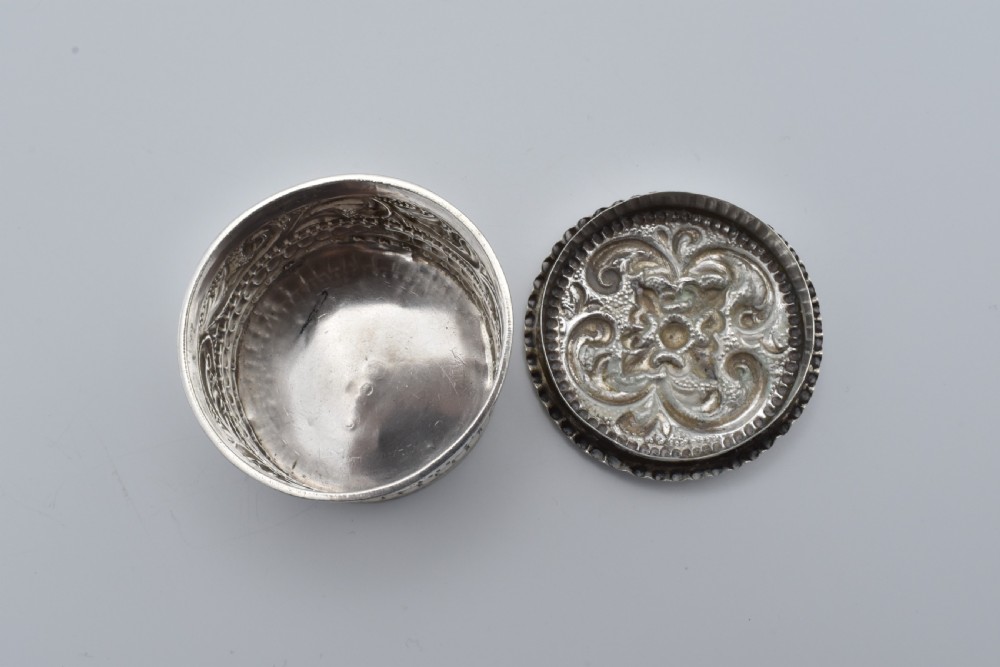 A circular Victorian sterling silver snuff box with repousse floral scrollwork on the lid and fluted sides. View VII
