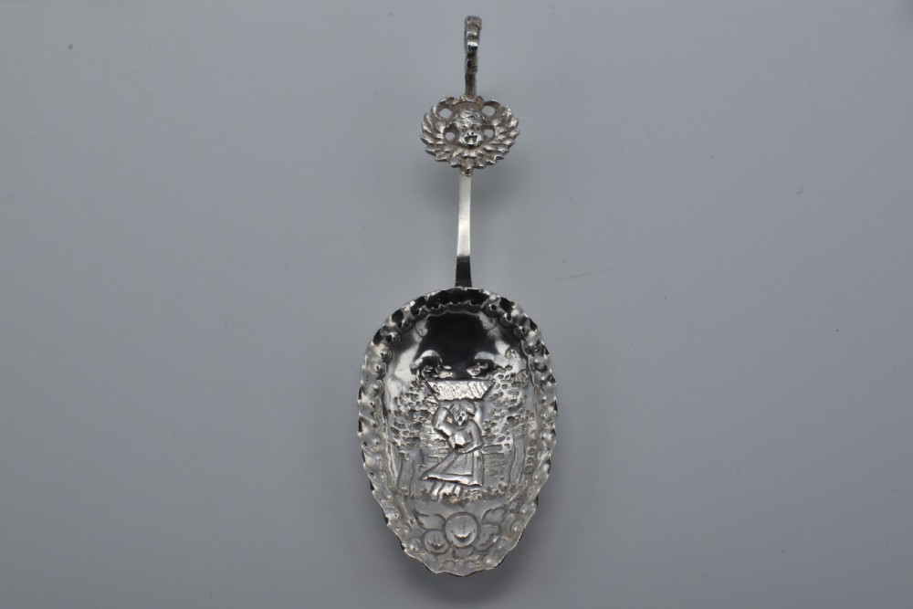 Victorian sterling silver caddy spoon featuring an embossed figurative scene in the scalloped bowl and a cherub mask terminal.