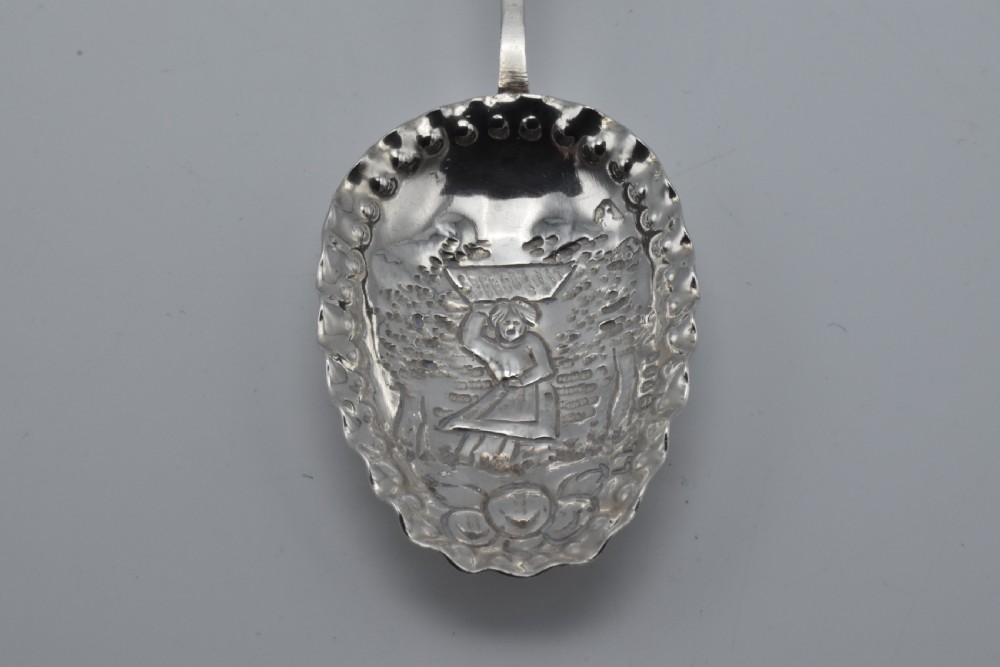 Victorian sterling silver caddy spoon featuring an embossed figurative scene in the scalloped bowl and a cherub mask terminal. View II