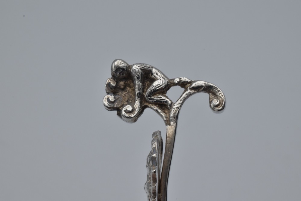 Victorian sterling silver caddy spoon featuring an embossed figurative scene in the scalloped bowl and a cherub mask terminal. View V