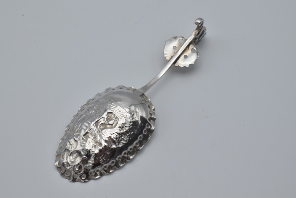Victorian sterling silver caddy spoon featuring an embossed figurative scene in the scalloped bowl and a cherub mask terminal. View VI