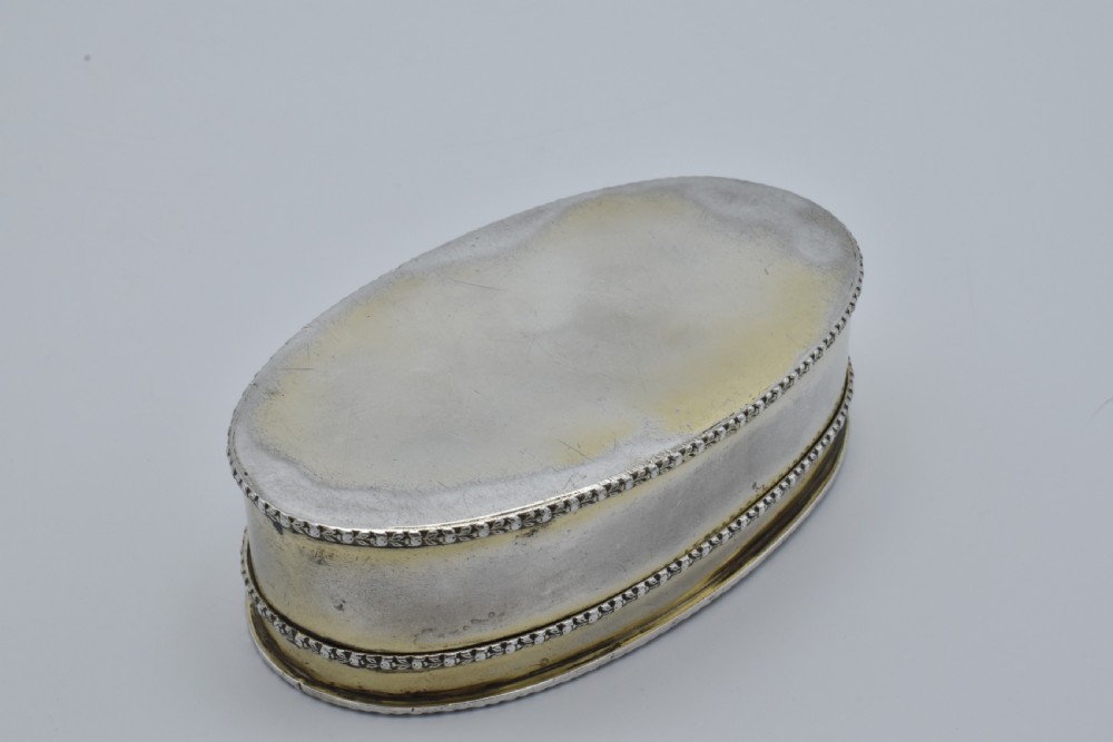 An oval antique sterling silver trinket box featuring engine-turned striped detailing on the lid, a central circular cartouche engraved with text, and beaded rims. View VII