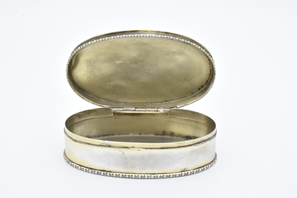 An oval antique sterling silver trinket box featuring engine-turned striped detailing on the lid, a central circular cartouche engraved with text, and beaded rims. View VIII