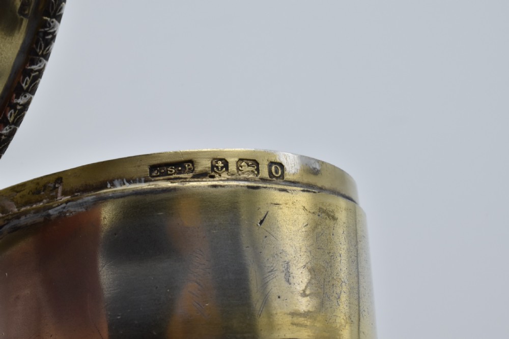 An oval antique sterling silver trinket box featuring engine-turned striped detailing on the lid, a central circular cartouche engraved with text, and beaded rims. View XI