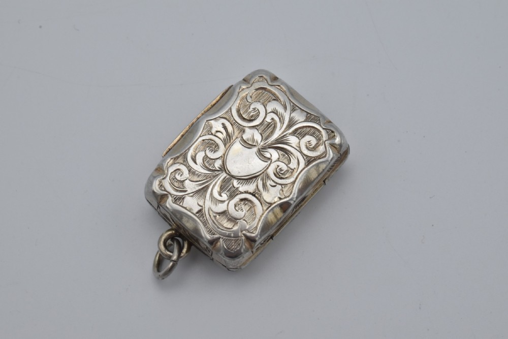 A small rectangular Victorian sterling silver vinaigrette featuring foliate engraving, a central shield cartouche, and a top suspension ring. View II