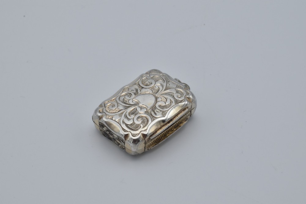 A small rectangular Victorian sterling silver vinaigrette featuring foliate engraving, a central shield cartouche, and a top suspension ring. View III
