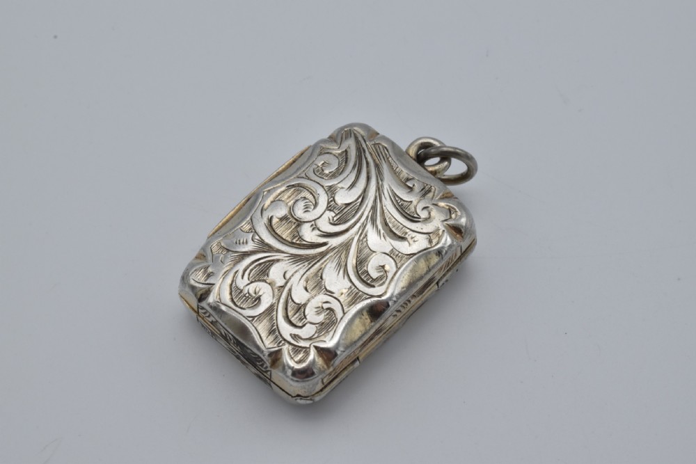 A small rectangular Victorian sterling silver vinaigrette featuring foliate engraving, a central shield cartouche, and a top suspension ring. View IV