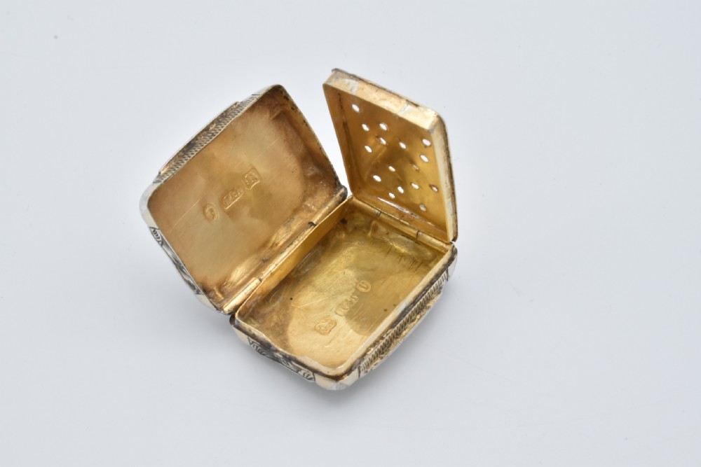 A small rectangular Victorian sterling silver vinaigrette featuring foliate engraving, a central shield cartouche, and a top suspension ring. View VII