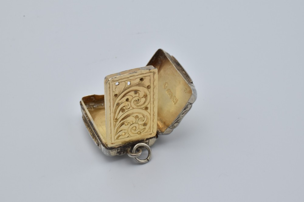A small rectangular Victorian sterling silver vinaigrette featuring foliate engraving, a central shield cartouche, and a top suspension ring. View VIII