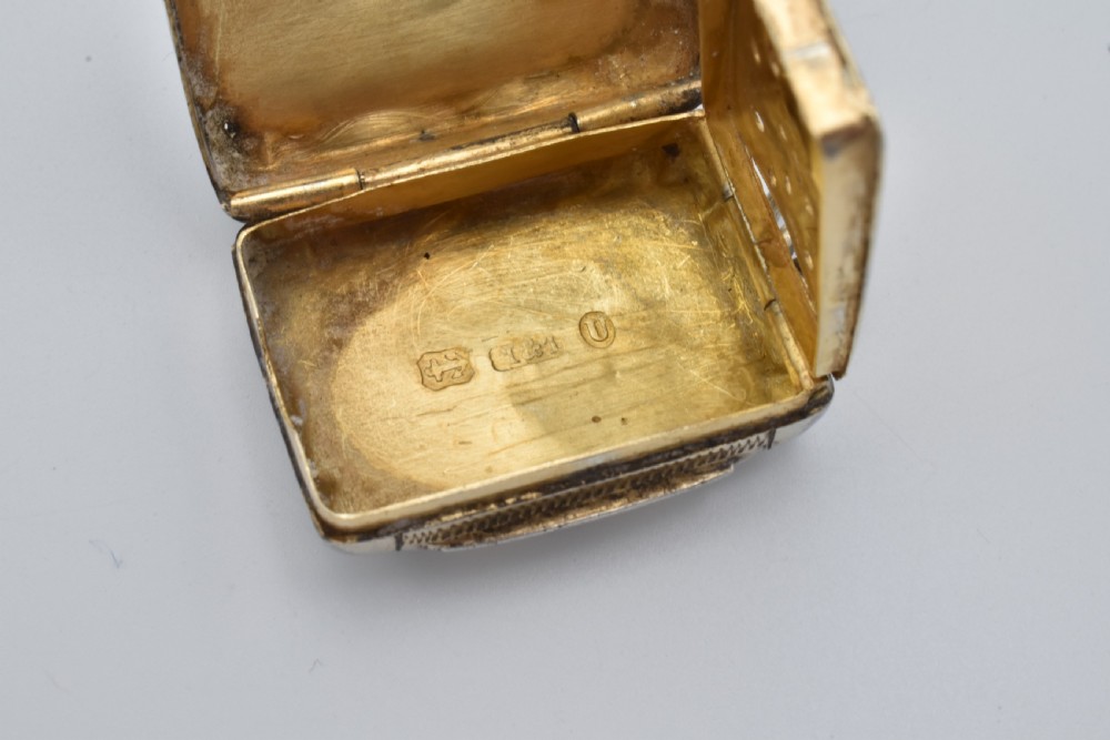 A small rectangular Victorian sterling silver vinaigrette featuring foliate engraving, a central shield cartouche, and a top suspension ring. View IX