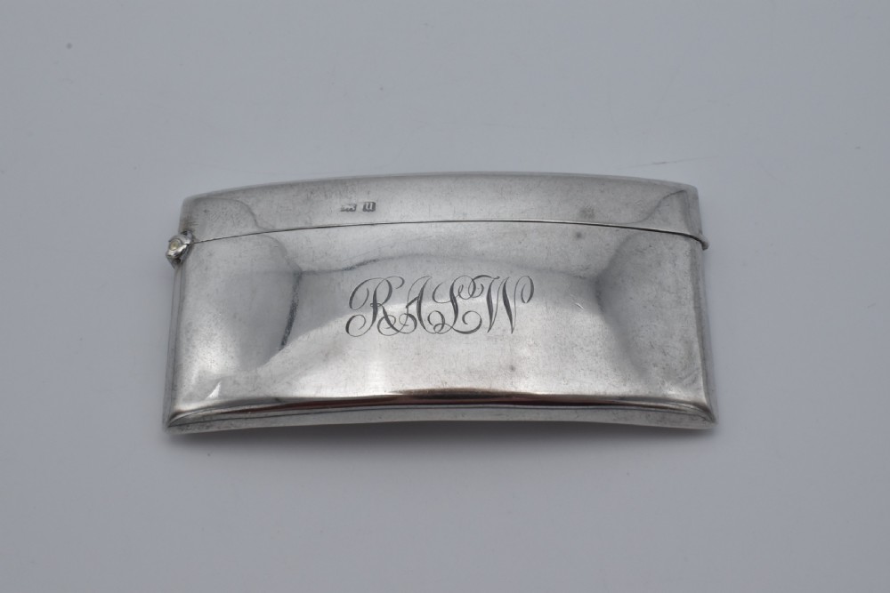 A curved sterling silver card case with hand-engraved monogram initials and visible British hallmarks near the top hinge.