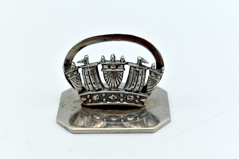A sterling silver menu holder shaped like a naval crown mounted on an octagonal silver base.
