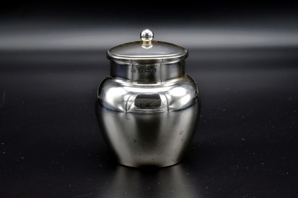 A small, bulbous sterling silver miniature tea caddy with a fitted lid, round ball finial, and visible British hallmarks stamped around the neck. View II