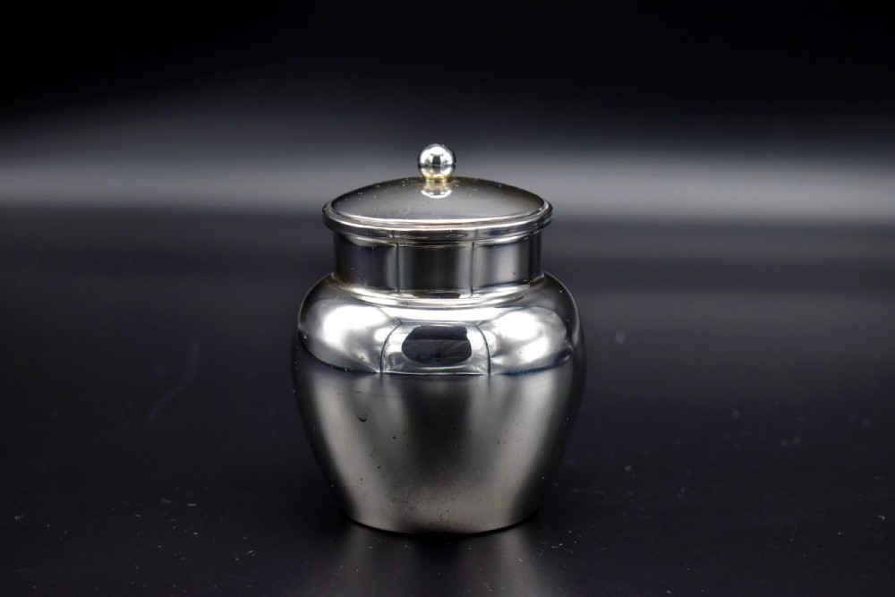 A small, bulbous sterling silver miniature tea caddy with a fitted lid, round ball finial, and visible British hallmarks stamped around the neck. View III