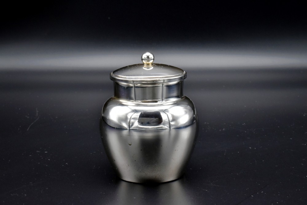 A small, bulbous sterling silver miniature tea caddy with a fitted lid, round ball finial, and visible British hallmarks stamped around the neck. View IV