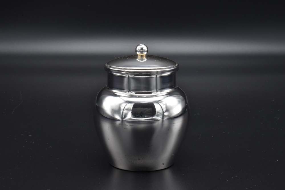 A small, bulbous sterling silver miniature tea caddy with a fitted lid, round ball finial, and visible British hallmarks stamped around the neck. View V